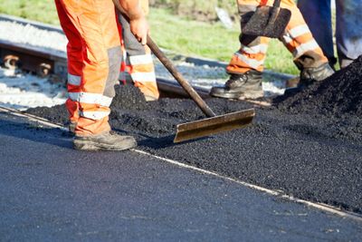 The contractors are putting a new layer of asphalt to the existing parking lot to create a new smooth, shiny black surface without having to replace it.